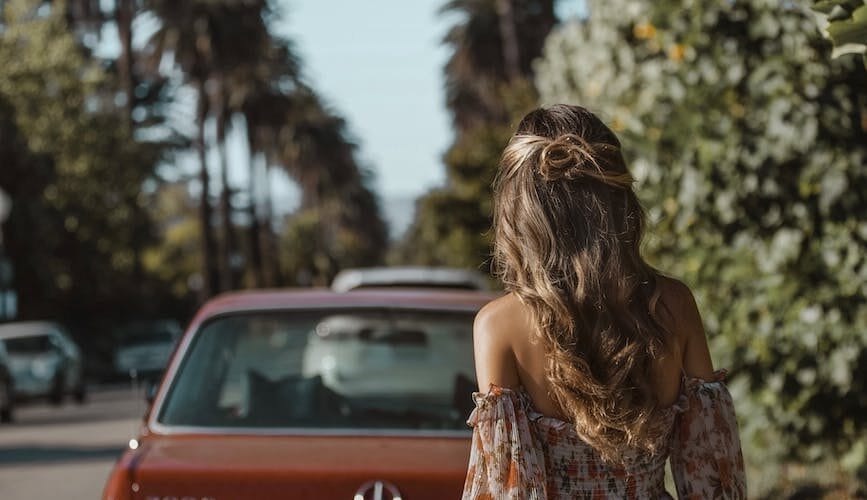 woman standing behind vehicle parked on side of road